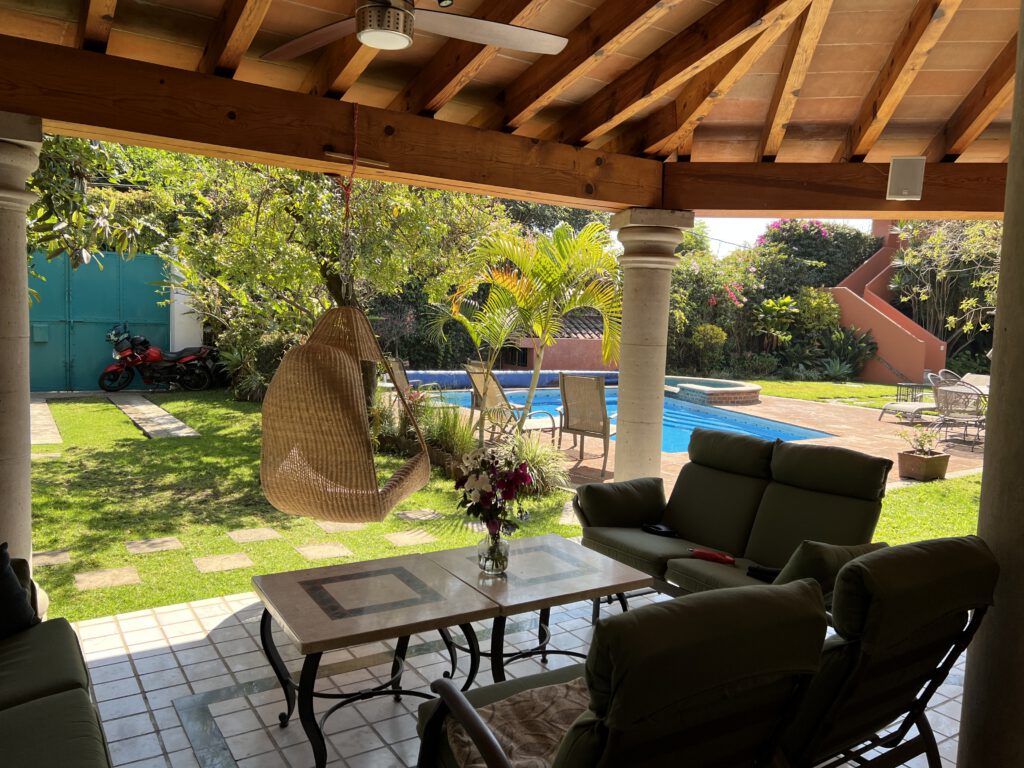 A covered terrace with seating, looking out over the garden and pool