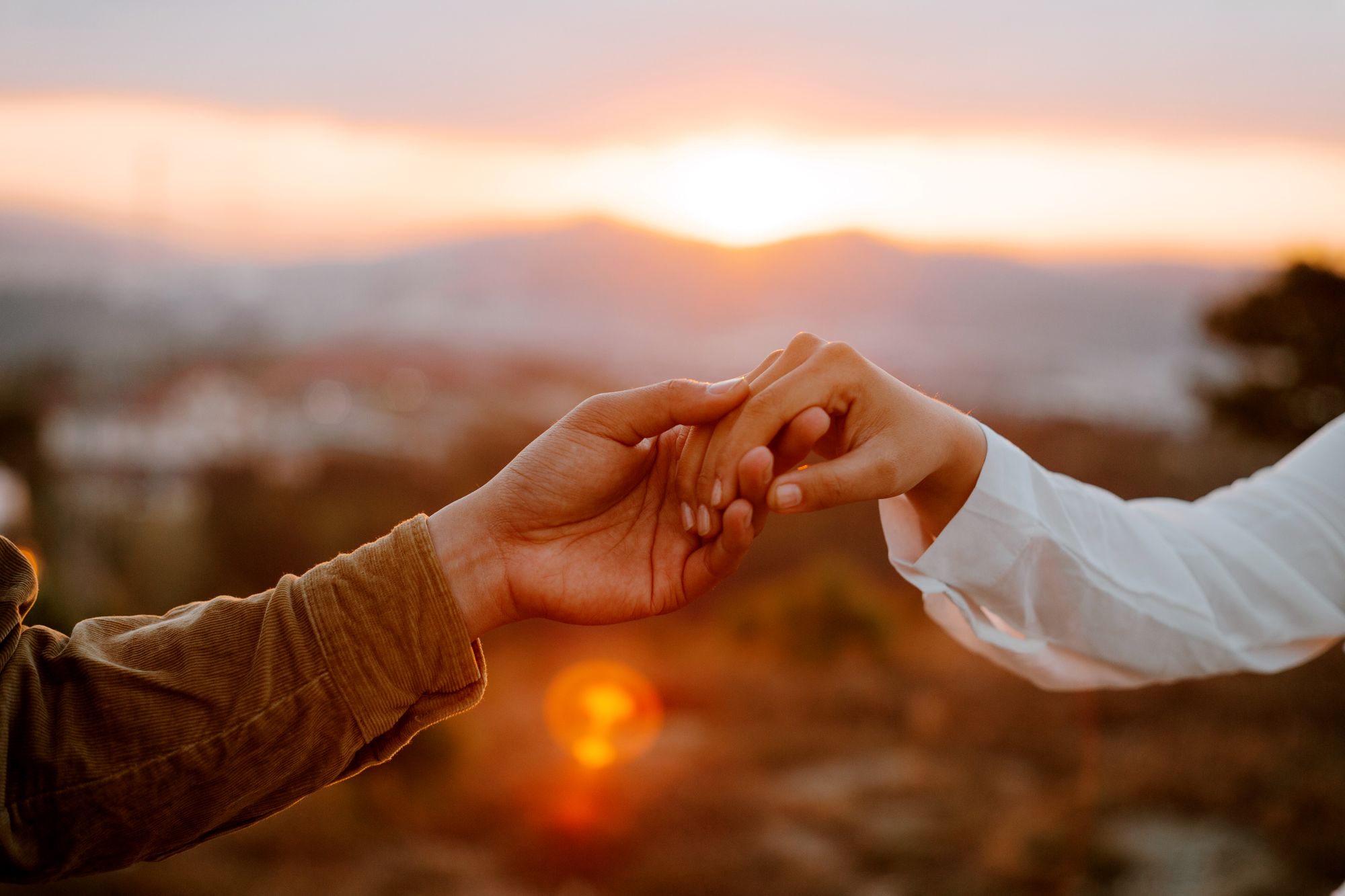 Two hands gently joined against a warm sunset