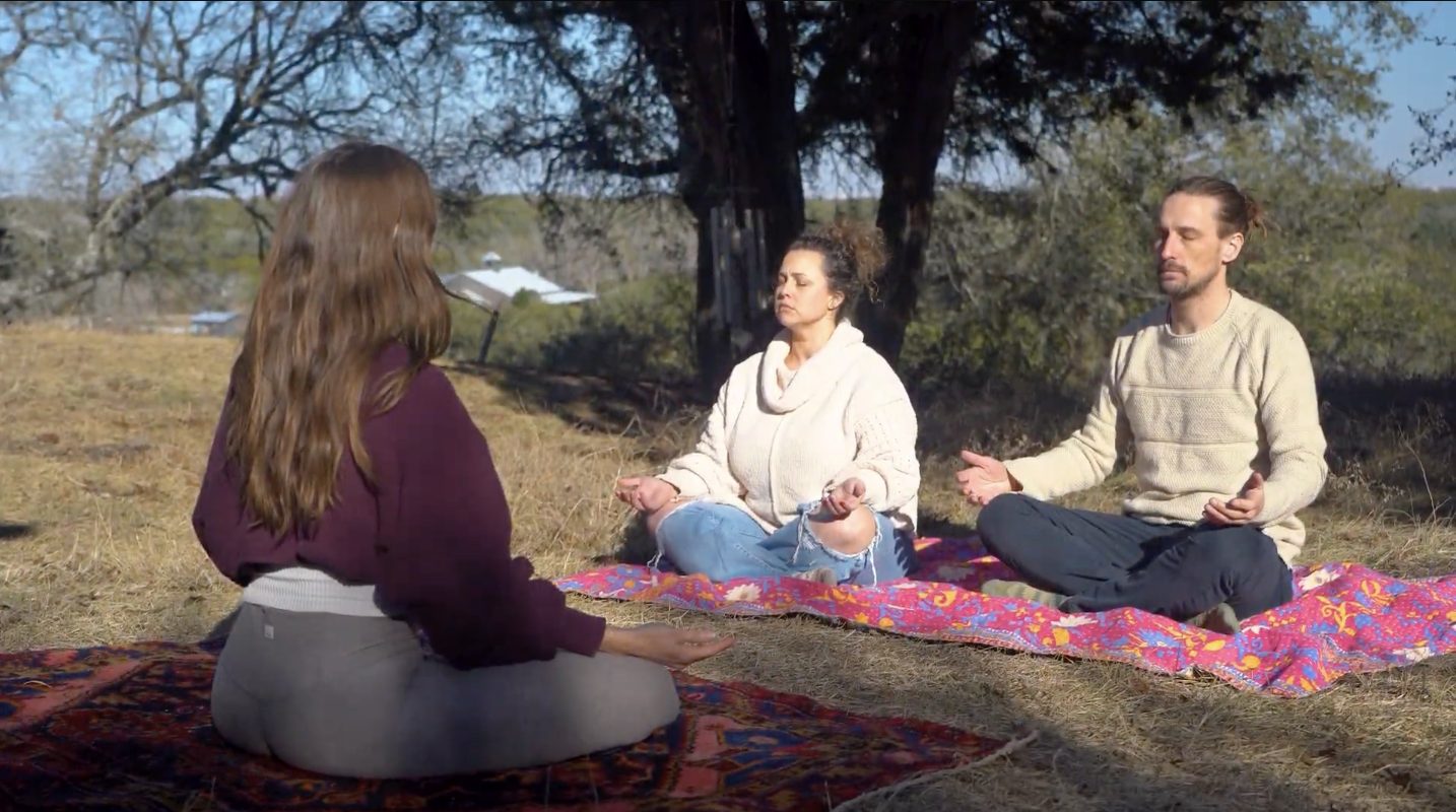 Guests and a coach meditating together on blankets beneath a Hill Country oak
